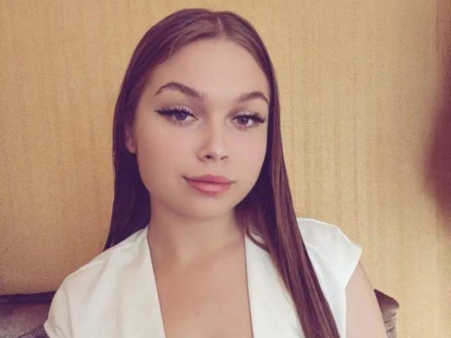 LaraPika has long brown hair, thick eyebrows, long eyelashes, pink lips, and wears a white shirt. Her face is centered, looking slightly to the left with a subtle smile.