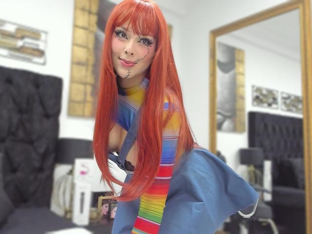 Alison Tatcher, con lunghi capelli rossi, una maglietta a righe colorate e una giacca blu, è china in avanti, mostrando il seno, con il trucco che include eyeliner e un piercing al labbro, in una stanza moderna..