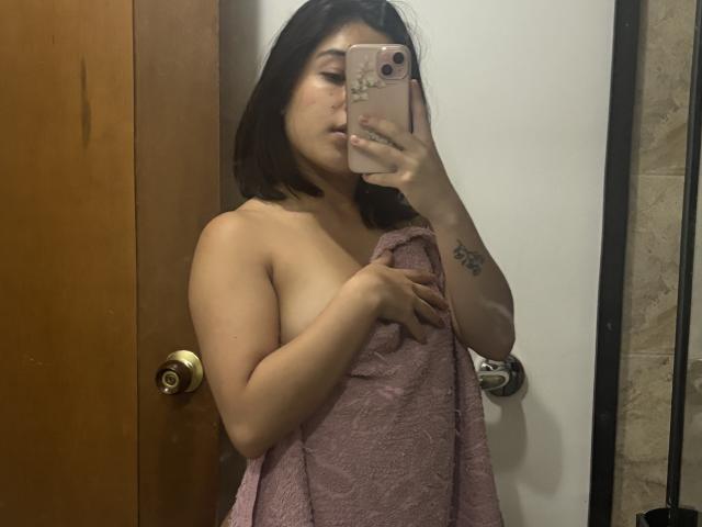 GiorginaR with medium brown skin and dark hair, holding a pink towel over her tits, taking a mirror selfie with a rose gold phone, showing a tattoo on her arm.