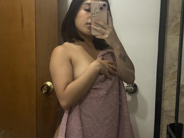 GiorginaR with a pink towel covering her tits, holding a phone in a mirror selfie, has short black hair and a tattoo on her right arm.