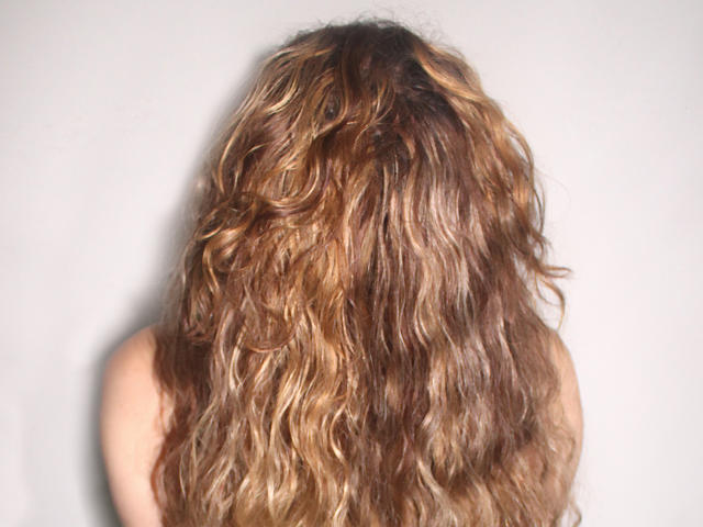 PriscillaHotMature's wavy, dirty blonde hair with brown highlights, covering her bare back, set against a plain white background.