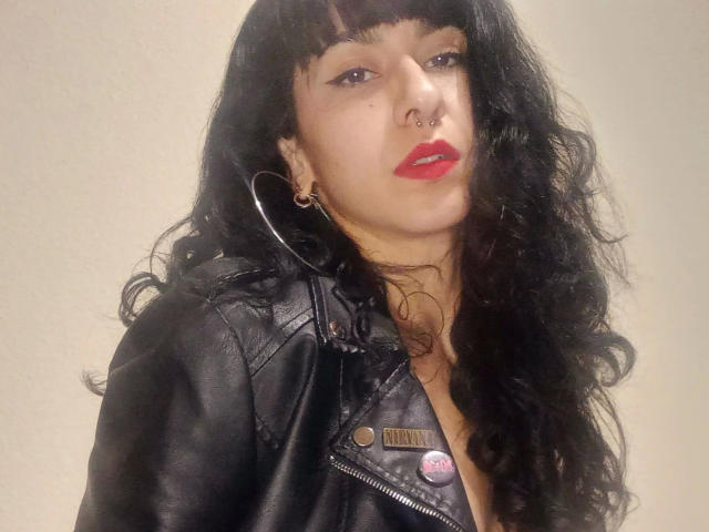 PandoraPurple-hot with black leather jacket, red lipstick, nose ring, hoop earrings, and long curly black hair. Boobs slightly visible under jacket. Neutral face with slight smirk.