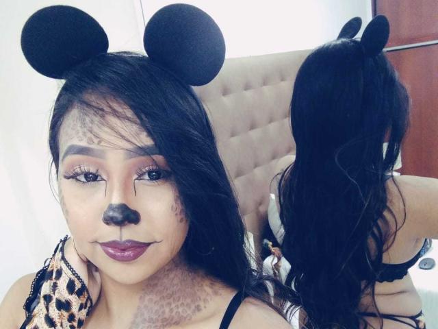AliciaRichie with black mouse ears, leopard print sleeve, and dark makeup, including black nose and teeth, in front of mirror, showing her back and long black hair.