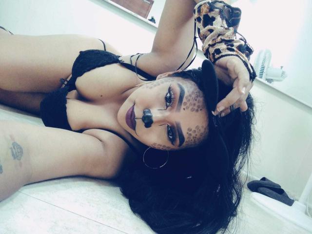 AliciaRichie lying on floor, wearing black lace bra, large tits, leopard print scrunchie, tattoos, dark makeup, hoop earrings, black hair, looking at camera, arm over head.
