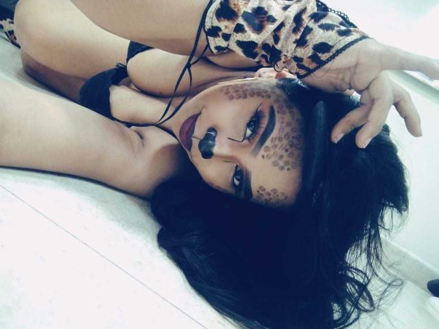 AliciaRichie with leopard print sleeves, lying on floor, black lingerie, painted leopard face, black hair, eye contact, head tilted, hand in hair, visible tits, sexy, seductive.
