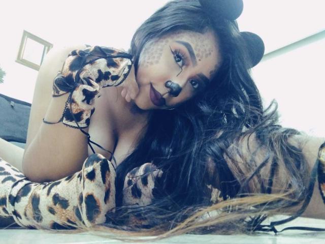 AliciaRichie with big tits, wearing a leopard print outfit and bear mask, laying on her stomach, her long brown hair in front, looking at the camera.