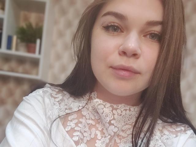 SophieApple with brown hair, white lace top, and pink lips, showing her face, slightly parted lips, and small nose. Her eyes are half-open, and she has a subtle smile.