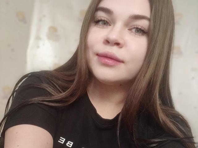 SophieApple has long brown hair, light skin, and pink lips, wearing a black shirt, with subtle eyeliner and natural makeup, looking at the camera with a slight smile.