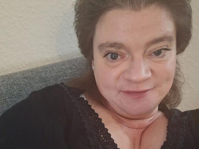 MollyBoobs-hot has a chubby face, brown eyes, and wears a black lace top. She's smiling slightly with her chest visible, showing a bit of cleavage.