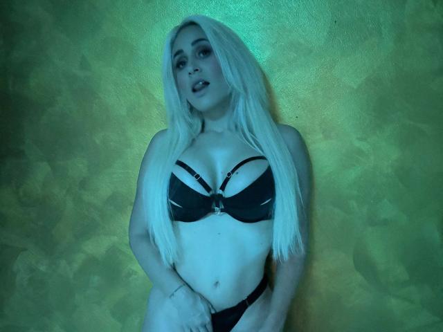 LunaSky-hot with long blonde hair, wearing a black bra with straps and black panties, standing with a blue-green glow, showing her tits and a slight view of her pussy.