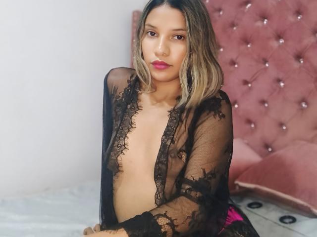 SashaChloe is wearing a sheer black lace robe, exposing her small tits, with her pink lips slightly parted and blonde hair falling to her shoulders.