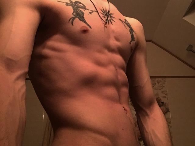NikkyBanny's muscular, tattooed, bare-chested torso with visible abs, nipples, and chest tattoos in dim, warm lighting. NikkyBanny has a necklace with a star-shaped pendant.