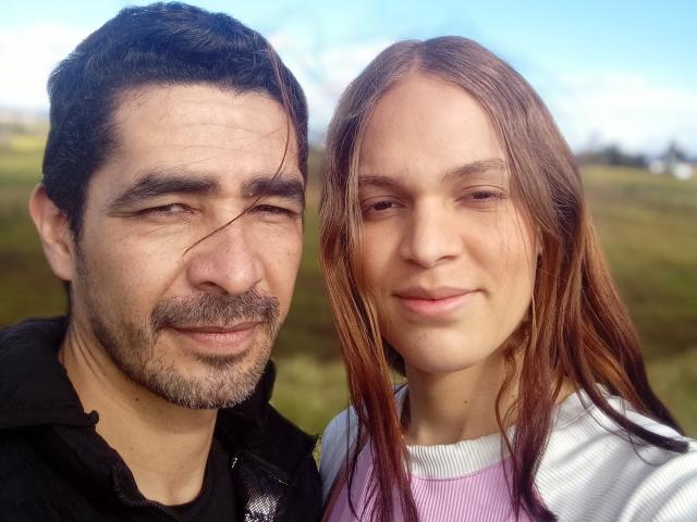 A CoulpleDark tem um cara de cabelo escuro com bigode, e a CoulpleDark tem uma garota de cabelo ruivo com cabelo liso. Ambos estão sorrindo, vestindo roupas casuais e estão ao ar livre..