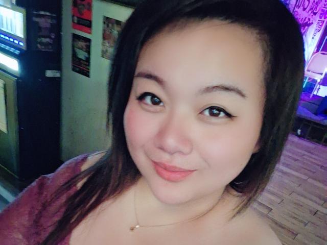 RoxyKay with medium brown skin, black straight hair, and cute pink lips, smiling softly at the camera, wearing a pink top, necklace, and subtle eyeliner.