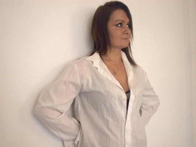 DoreenSexy has brown hair, a white button-up shirt, hands in pockets, looking to the side, with a necklace, and a slightly open shirt showing her tits.
