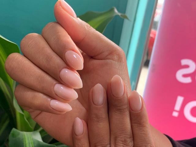 CarlaMuille's hands with glossy, pink-tinted, almond-shaped nails, showing off her neatly manicured fingers and slightly tanned skin. Her nails are shiny and well-cared-for.