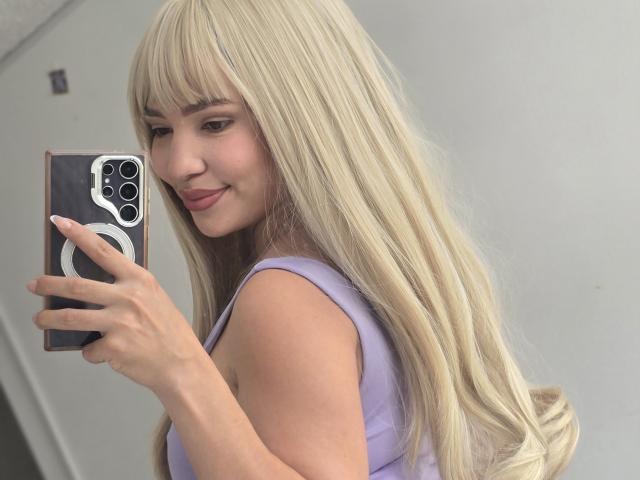 KendallPiierce69 with long blonde hair, smiling at a mirror selfie, holding a phone with a ring grip, wearing a purple top, showing her ass.