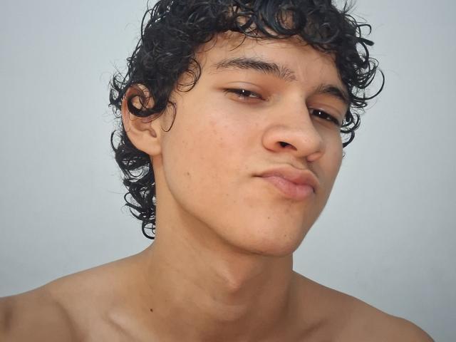 SamuelHills has curly black hair, light brown skin, and a neutral expression with slightly pouted lips. He's shirtless with a smooth, bare neck.