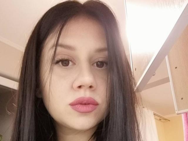 SamanthaApple has pale skin, brown eyes, black straight hair, and pink lipstick. She's looking directly at the camera with a neutral expression. Her nose is small and cute.