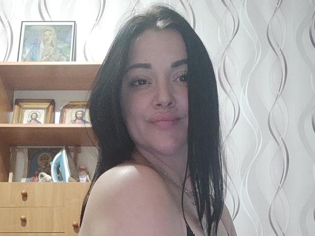 XCrazyBabeX has long black hair, a nose ring, and is smiling with pink lips. She's showing her bare shoulder, with her tits slightly visible. She's looking at the camera.