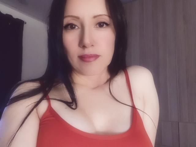 MondBlue with pale skin, black hair, and red lipstick, wearing a red tank top, showing her tits, has a neutral expression, and is centered in the image.
