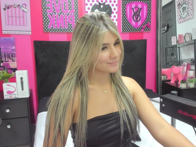 SashaPolet has long, straight blonde hair, tan skin, and is wearing a black strapless top, smiling with a subtle nose ring, and a small gold necklace.
