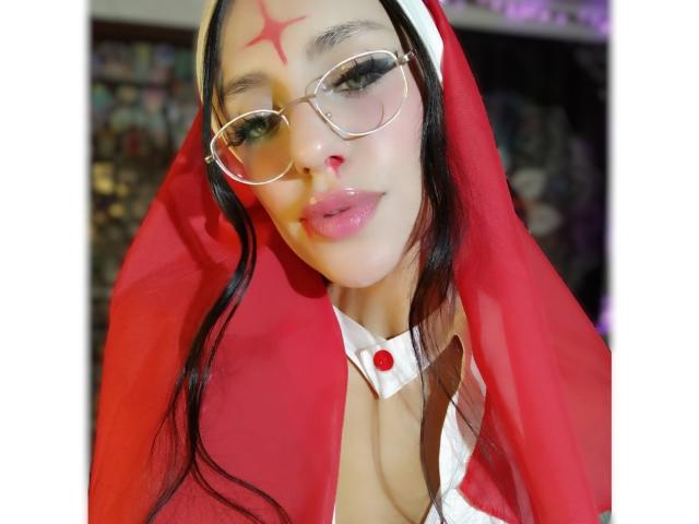 EroticAlexa in a red nun outfit with glasses, a red cross on her forehead, and a white collar, showing her tits. She has long black hair and glossy lips.