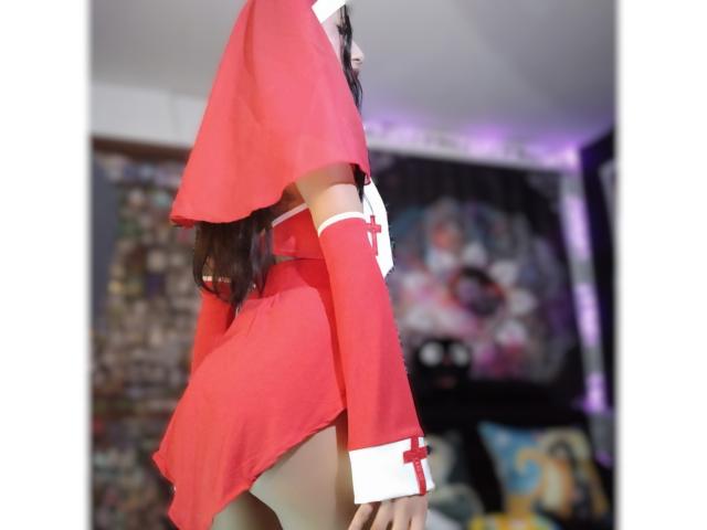 EroticAlexa in a red nurse outfit with white cross details, showing her ass and thigh, wearing a short skirt and arm sleeves, in a blurry room.