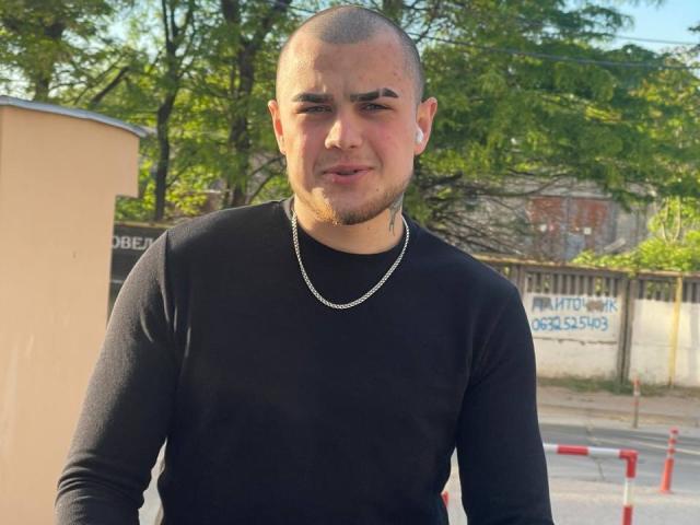 RichardSexy, bald with a goatee, wearing a black long-sleeve shirt and silver chain, standing outdoors, looking slightly annoyed with eyebrows raised.