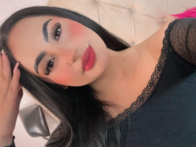 MartinaMendezz with long black hair, thick eyebrows, pink blush, red lipstick, black lace top, and hand in hair, showing off her sexy face and cute nose ring.
