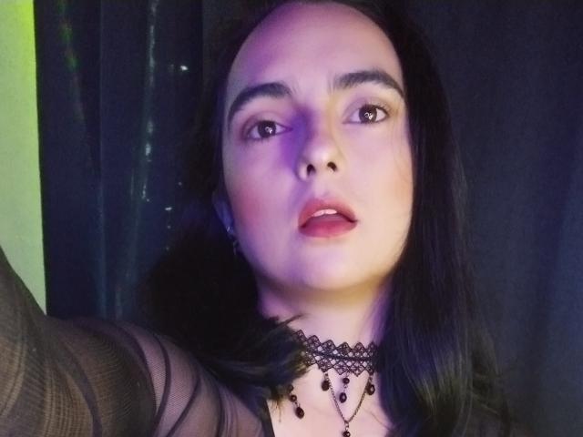 CandyParis ha la pelle chiara, i capelli neri e indossa un collare di pizzo nero con perline pendenti. Le sue labbra sono leggermente socchiuse e ha un'espressione seria..