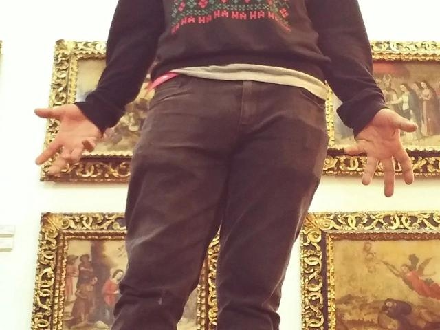 davydwolf-hot standing with hands out, wearing black sweatshirt and brown pants, showing ass, gold-framed paintings in background.