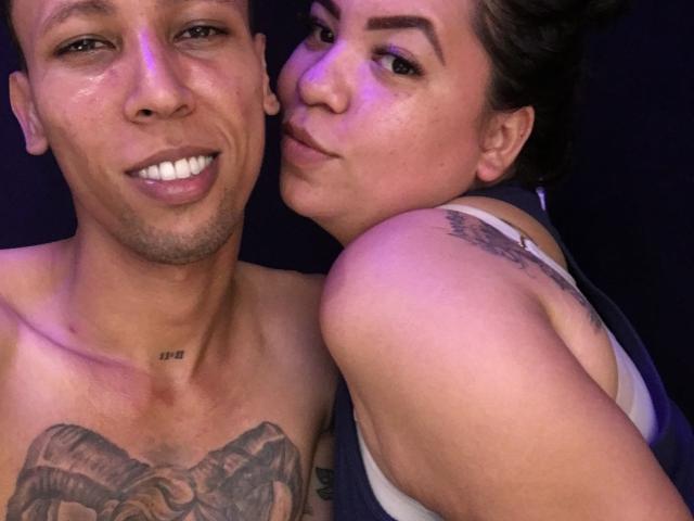 ElChicletv with tattoos, shirtless, and ElChicletv with tattoos, in a tank top, leaning in, smiling, purple light, visible ram tattoos on ElChicletv's chest, ElChicletv's shoulder tattoo.