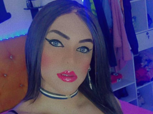 GeishaSenier with shiny red lips, blue eyes, thick eyebrows, long brown hair, wearing a choker, looking at the camera in a blue-lit room. Boobs not visible.