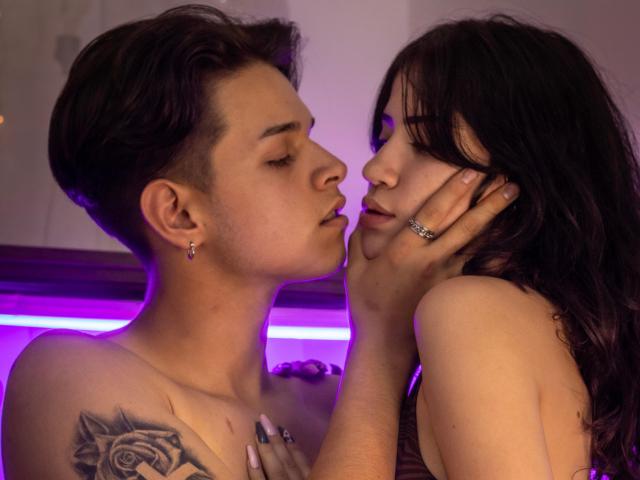 JadeAndLeo with short brown hair and a tattoo, kissing forehead, holding face of dark-haired JadeAndLeo with purple neon light, both topless, intimate, purple glow.