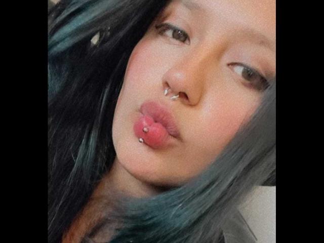 LilithAbrahel69 has dark green hair, brown eyes, and a nose piercing. Her pink pout is adorned with a lip piercing. She's puckering her lips in a selfie.