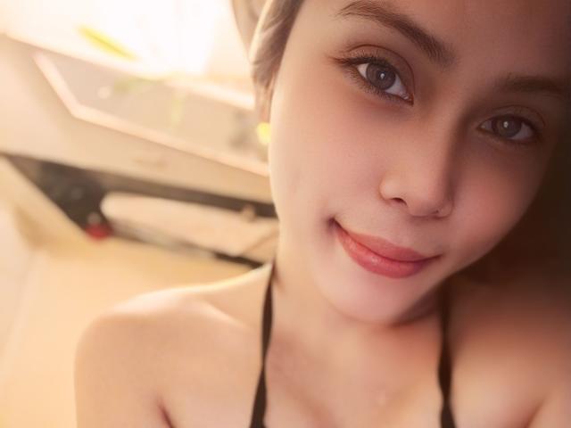 TSAnabelleSwift con una sonrisa encantadora, ojos azules y un top de tirantes negros, mostrando sus hombros desnudos y un ligero bronceado, en un selfie con una iluminación suave..