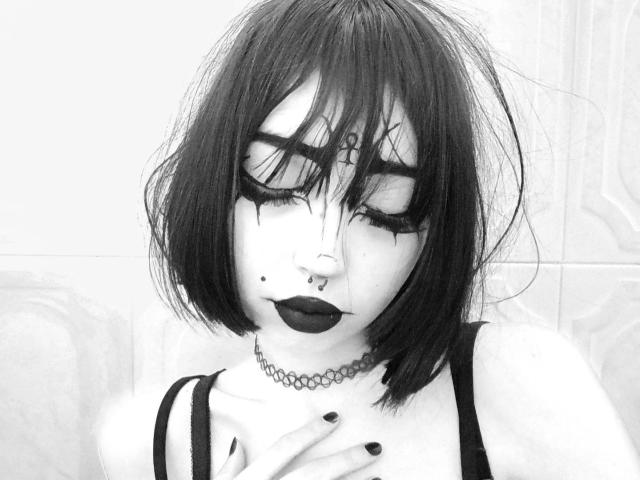 SilencePhsi, con el pelo negro y despeinado, ojos cerrados y delineador de ojos marcado. Tiene lápiz labial oscuro, un piercing en la nariz y un collar. Su mano descansa sobre su pecho, mostrando uñas negras..