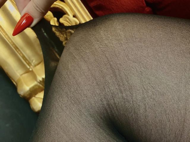 LexyClaire's black mesh panty-covered ass, showing a tight weave, with a red manicured finger gently pulling the fabric to the side. Golden chair in background.