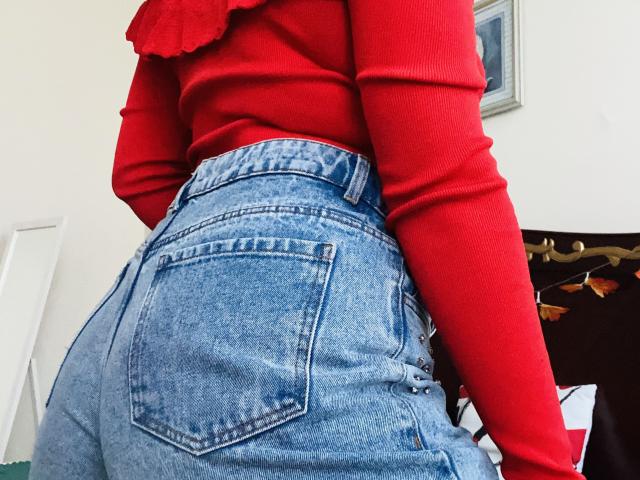 KarKutie's ass in high-waisted blue jeans, wearing a red long-sleeve top with a ruffle, standing with her back to the camera.