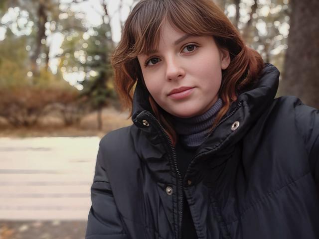 StaceyLex has medium brown hair, fair skin, and is wearing a black puffy jacket with a gray turtleneck. She's looking at the camera with a slight smile.