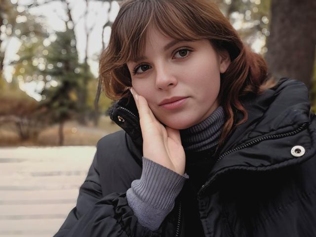 StaceyLex with brown hair, looking at the camera, wearing a black puffy jacket and gray turtleneck, hand on cheek, soft smile, bokeh forest background, natural light.