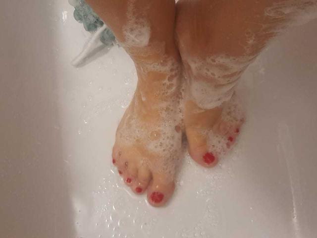 ElizabethRaegan's soapy feet with red toenails in a white bathtub, covered in bubbles, standing with toes slightly apart.