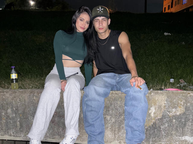 SofiaAndgeordi, con il seno visibile attraverso una maglietta verde, pantaloni bianchi e capelli neri, seduta su cemento, con Geordi che indossa una maglietta nera senza maniche, jeans blu e un berretto verde. Una bottiglia di birra..