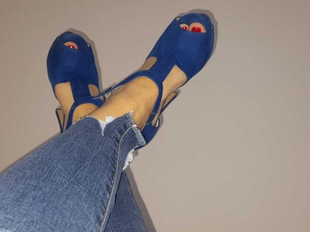 ElizabethRaegan's legs in blue ripped jeans with visible frays, wearing blue open-toe high heels showing red nail polish on toes, legs crossed.