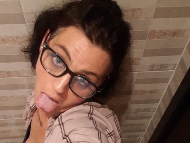 Decva69 has short dark hair, black glasses, and is sticking out their tongue with a goofy expression. They're wearing a pink plaid shirt, and their blue eyes are visible.