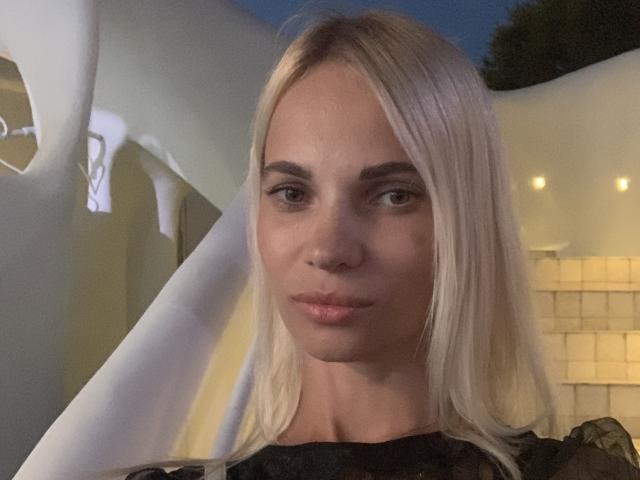 DonorDi has blonde hair, light skin, and is looking at the camera with a slight smile. She's wearing a black top, and the photo is taken at night.