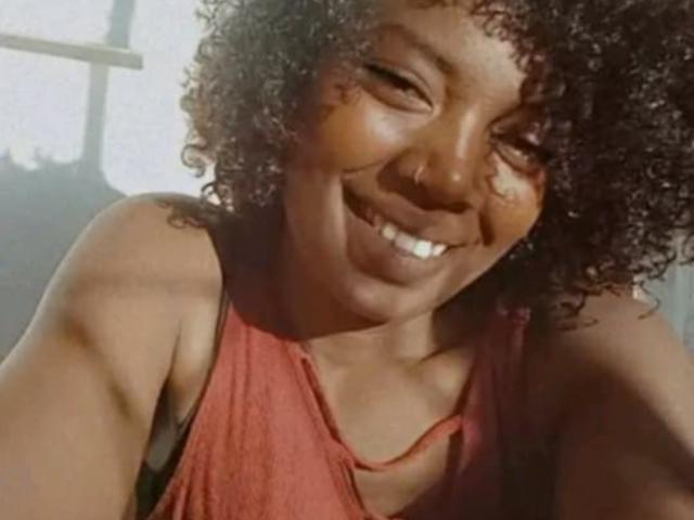 JessicaBella69 with curly brown hair, smiling with teeth showing, wearing a red tank top, has a nose ring, and a tattoo on her right shoulder.