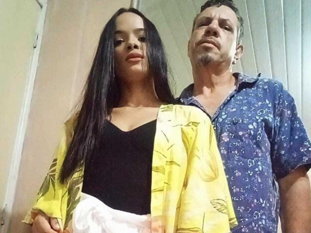 HoneyJeffCouple, una donna alta con lunghi capelli neri e piccoli seni, indossa una camicetta gialla con fiori e un top nero senza maniche. HoneyJeffCouple, un uomo con la barba, indossa una camicia blu a motivi..