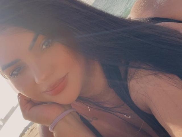 JessicaXSexy has long dark hair, light blue eyes, and a slight smile. She's wearing a black top, resting her chin on her hand, showing her smooth, pale skin.